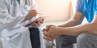 a patient holding their hands in front of a doctor writing on a notepad