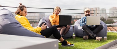 3 individuals sitting in bean bags working on laptops in a rooftop lounge