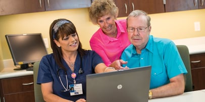 a nurse showing two older individuals information on a laptop 